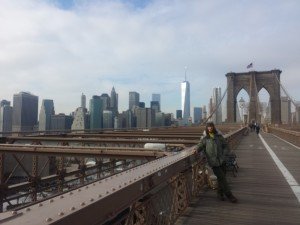 Mikey standing on the Brooklyn Bridge with the Manhatten skyline in the background