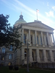 A government building is capitaled lady liberty atop a dome. It also flies the American flag. Juxtiposed in the front of the building is a pole with several survalence cameras pointed in several directions.