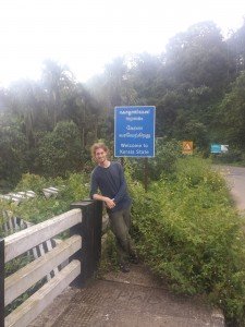 Mikey stands on a bridge next to a sign that reads "Welcome to Kerala State"