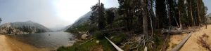 Panorama shot shoing Mikey standing on a high-sierra beach next to a lush, green forest