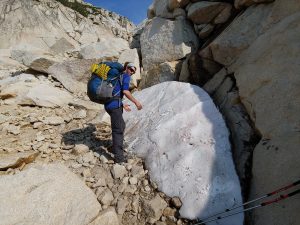 Mikey is standing next to a big patch of snow in amongst a pile of rocks.