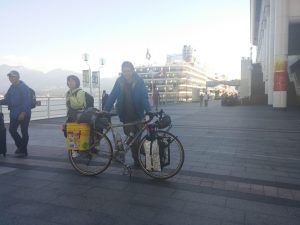 Mikey stands smiling with his fully-loaded bicycle in front of the cruise ship