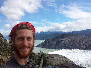 Mikey is smiling in a selfie. Behind him is the terminus of glacier grey as it meets a lake.