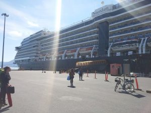 The huge Noordam ship is shown docked. 50m before the ramp for boarding the ship, Mikey's bicycle leans against a sign and S stands in awe of the ship.