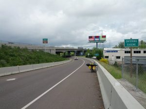 Mikey's bicycle is in the shoulder leaned up against a concrete barrier. A sign reads "ENTERING EUGENE"