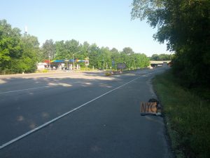 A backpack is sitting in the shoulder of an on-ramp with a cardboard sign reading "NYC". A sign indicates that the on-ramp is Interstate 95.