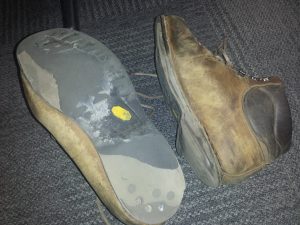A pair of dry & worn-out boots are shown. The rubber is heavily worn down and missing in places.