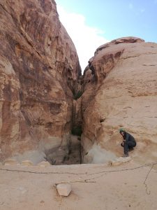 Mikey stands atop a man-made wall built at the edge of a canyon. In front of them is barbed wire.