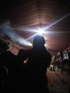 Mikey is silhouetted in a bedouin tent. He is exhaling smoke from a nargileh.