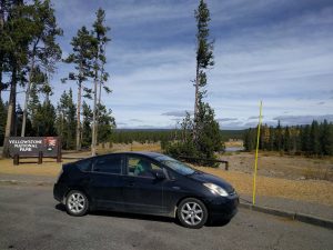 Mikey's car is parked along-side a sign that reads "Yellowstone National Park"