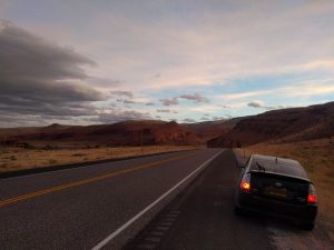 Mikey's car is parked in the shoulder. In the distance are beautiful reddish canyons