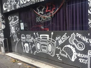 Picture shows a storefront for a club. The window reads "Rocket Bar & Music" and "100% vegano".