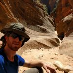 Mikey sits in a dry canyon bottom. The canyon's walls have been shaped by wind & rain into a beautiful winding shape.