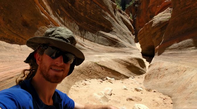 Mikey sits in a dry canyon bottom. The canyon's walls have been shaped by wind & rain into a beautiful winding shape.