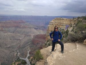 Mikey is smiling, standing near a cliff. Behind him is a natural bridge, and reddish canyons that make up the Grand Canyon.