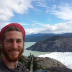 Mikey is smiling in a selfie. Behind him is the terminus of glacier grey as it meets a lake.