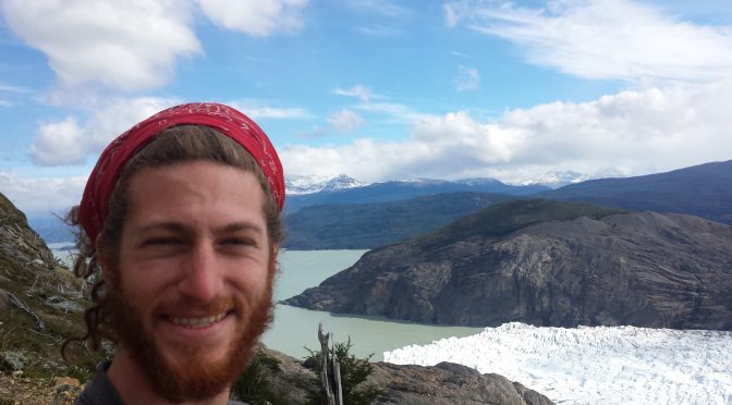 Mikey is smiling in a selfie. Behind him is the terminus of glacier grey as it meets a lake.