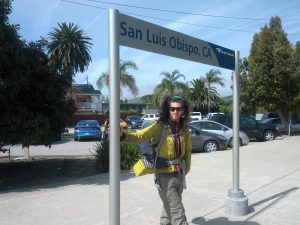 Mikey stands under an Amtrak sign designating the stop for "San Luis Obispo, CA"