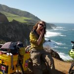 Mikey is shown sitting on a rock next to his bicycle. Behind him is a cliff overlooking the Pacific Ocean.