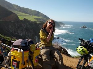 Mikey is shown sitting on a rock next to his bicycle. Behind him is a cliff overlooking the Pacific Ocean.