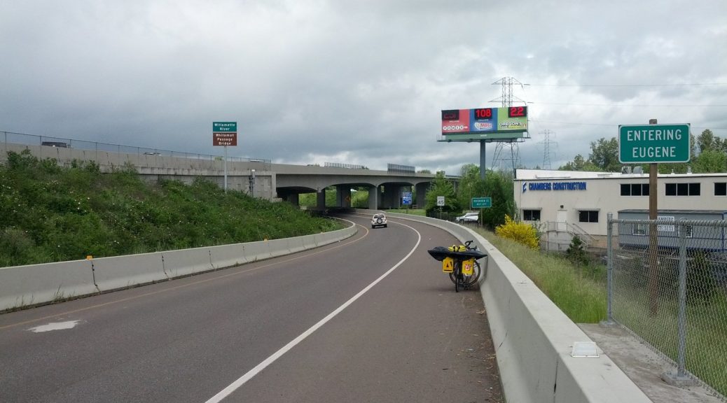 Mikey's bicycle is in the shoulder leaned up against a concrete barrier. A sign reads "ENTERING EUGENE"