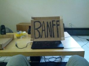 A POV shot shows a huge cardboard box with "BANFF" written on it in permanent marker.The sign is leaned-up against Mikey's laptop.