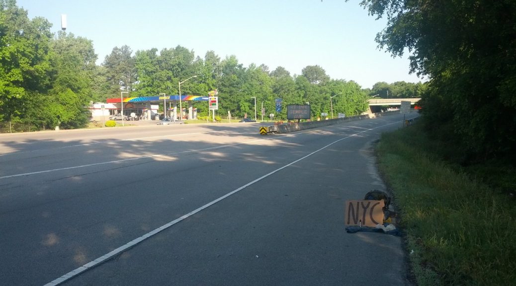 A backpack is sitting in the shoulder of an on-ramp with a cardboard sign reading "NYC". A sign indicates that the on-ramp is Interstate 95.