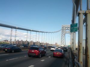 A suspension bridge with many lanes of cars. A sign hangs that reads "Welcome to NEW YORK. THE EMPIRE STATE."