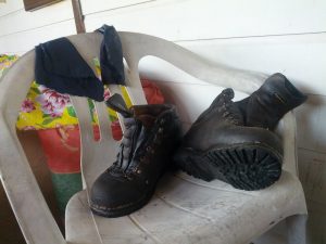 A pair of boots with new, thick soles rest on a plastic chair. Two blue rags are strung across the top of the chair.