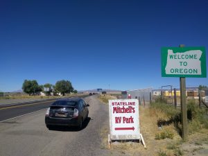 Mikey's car is parked next to a sign that reads "WELCOME TO OREGON"