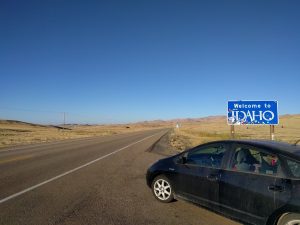 Mikey's car is parked next to a sign that reads "Welcome to IDAHO"