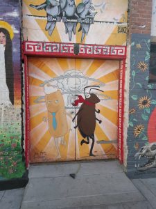 A doorway is painted with a picture of a twinkie and a cockroach holding hands & smiling as they run together away from a mushroom cloud