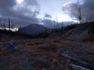 Mikey's tent is setup in a field. There is a large mountain in the distance, and the clouds cast picturesque shadows.