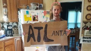 Mikey stands holding a cardboard sign that reads "ATLanta"