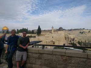 D & Mikey stand against a railing in the old city of Jerusalem. Behind them, the Al-Aqsa mosque and Dome of the Rock can be seen atop the Temple Mount.