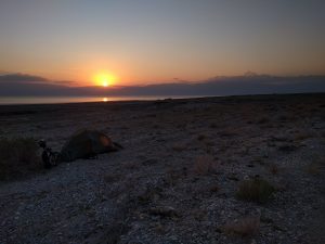 Mikey's tent is setup on the sands of the Dead Sea--with his Brompton Bicycle folded-up next to it. In the distance, the Dead Sea reflects the brilliant colors of the setting sun, which is just falling behind the mountains in Jordan.