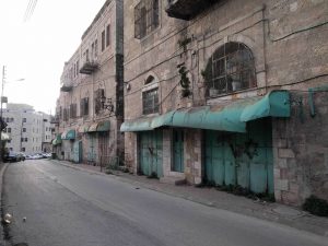 A street is lined with entrances to homes & shops. The doors to the homes are copper-green and rusted. The doors have been welded shut, and tagged with spray-painted stars of David--ironically & ashamedly reminiscent of swastikas.